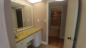 Une salle de bain dotée d’un comptoir en granit, d’un grand miroir et d’un dressing avec un plancher en bois.