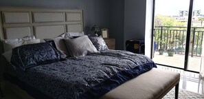 Une chambre avec un grand lit, une table de chevet, une lampe et une vue sur l’extérieur.