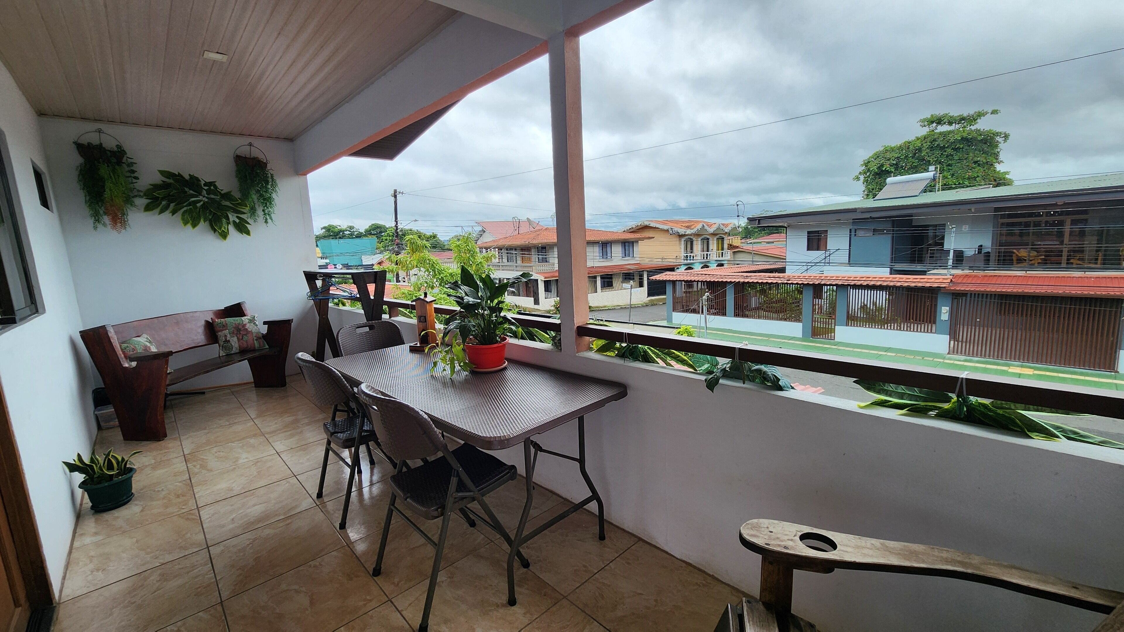 A balcony with a table and chairs, potted plants, and a view of neighboring houses.