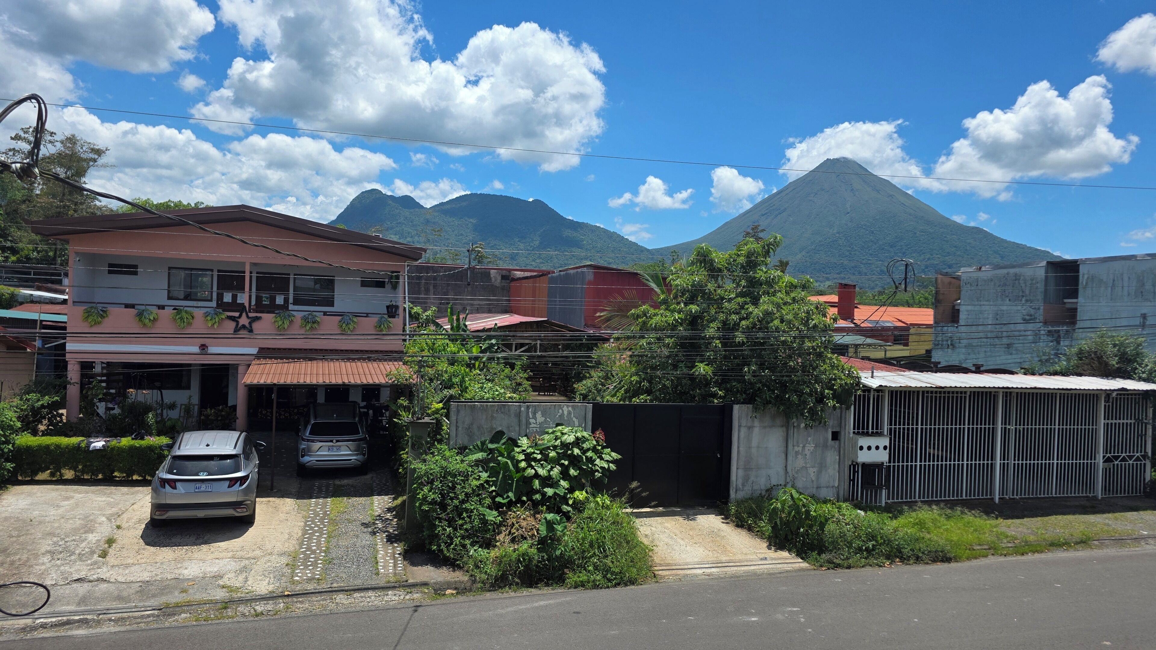 Ein Gebäude mit rotem Dach, ein Parkplatz mit zwei Autos und ein Berg im Hintergrund.