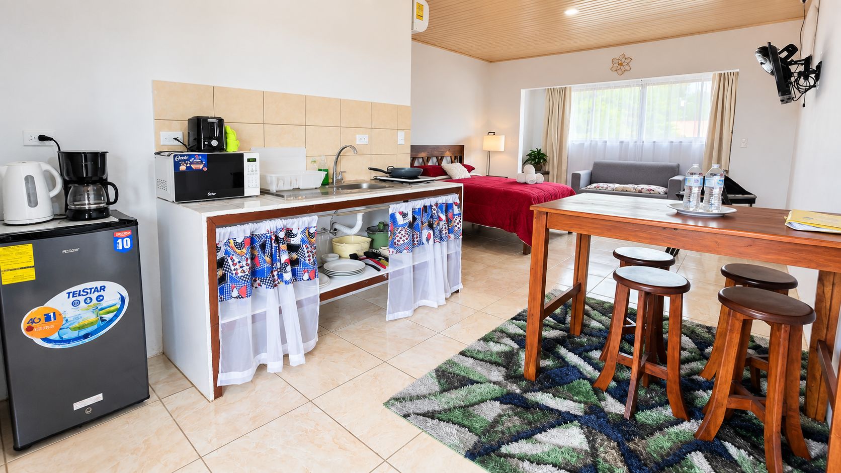 Una habitación de hotel compacta con kitchenette, zona de comedor y cama.