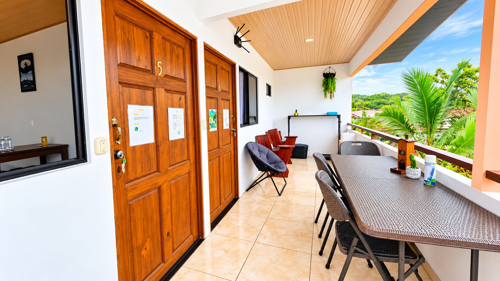 Une chambre d’hôtel avec une porte en bois, un balcon doté d’une table et de chaises, et une vue sur la verdure.