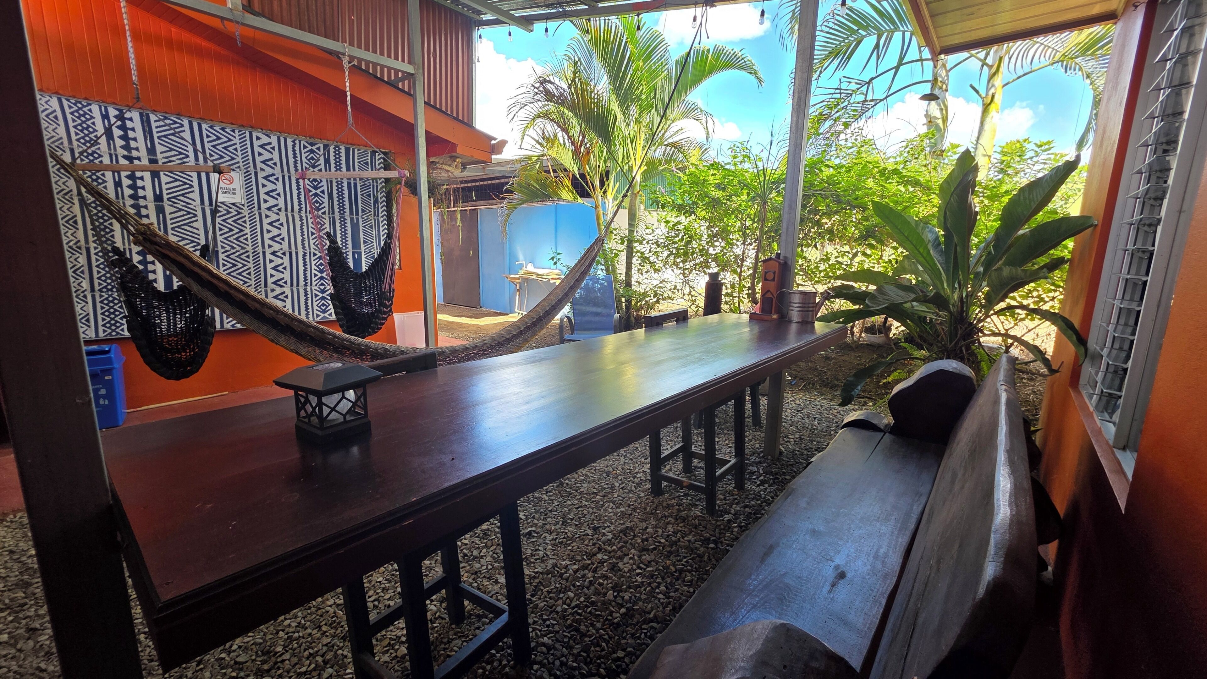 Une table en bois, un hamac, un banc et un mur orné de motifs.