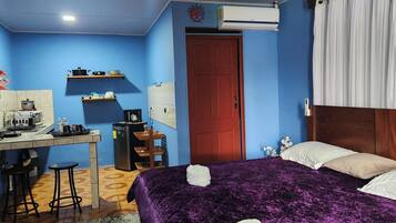 Ein Schlafzimmer mit Bett, Schreibtisch mit Stuhl, Kühlschrank, Waschbecken und einer roten Tür.