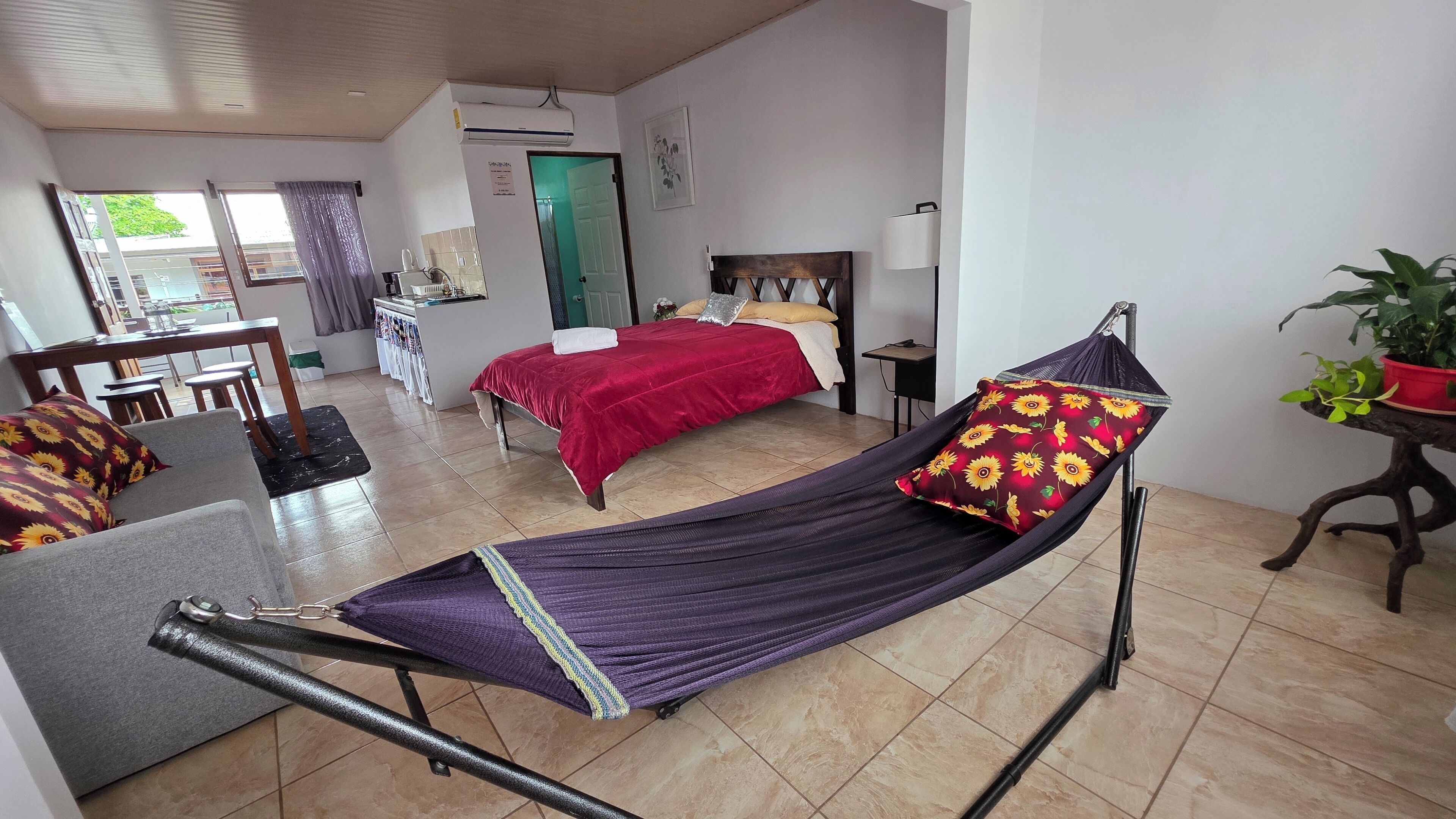 Una habitación con una cama, un sofá, una mesa de comedor y una mesita de noche con una lámpara.