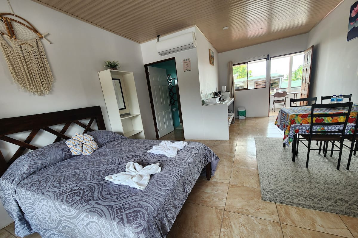 A hotel room with a bed, a dining area, and a view of the outside.
