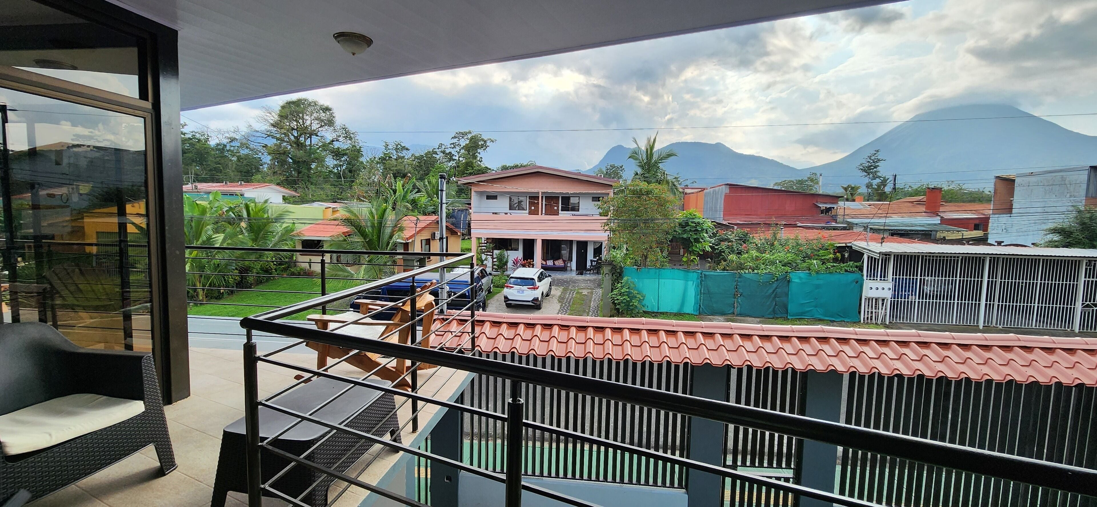 A balcony with a view of a residential area, a mountain in the background, and a parked car.