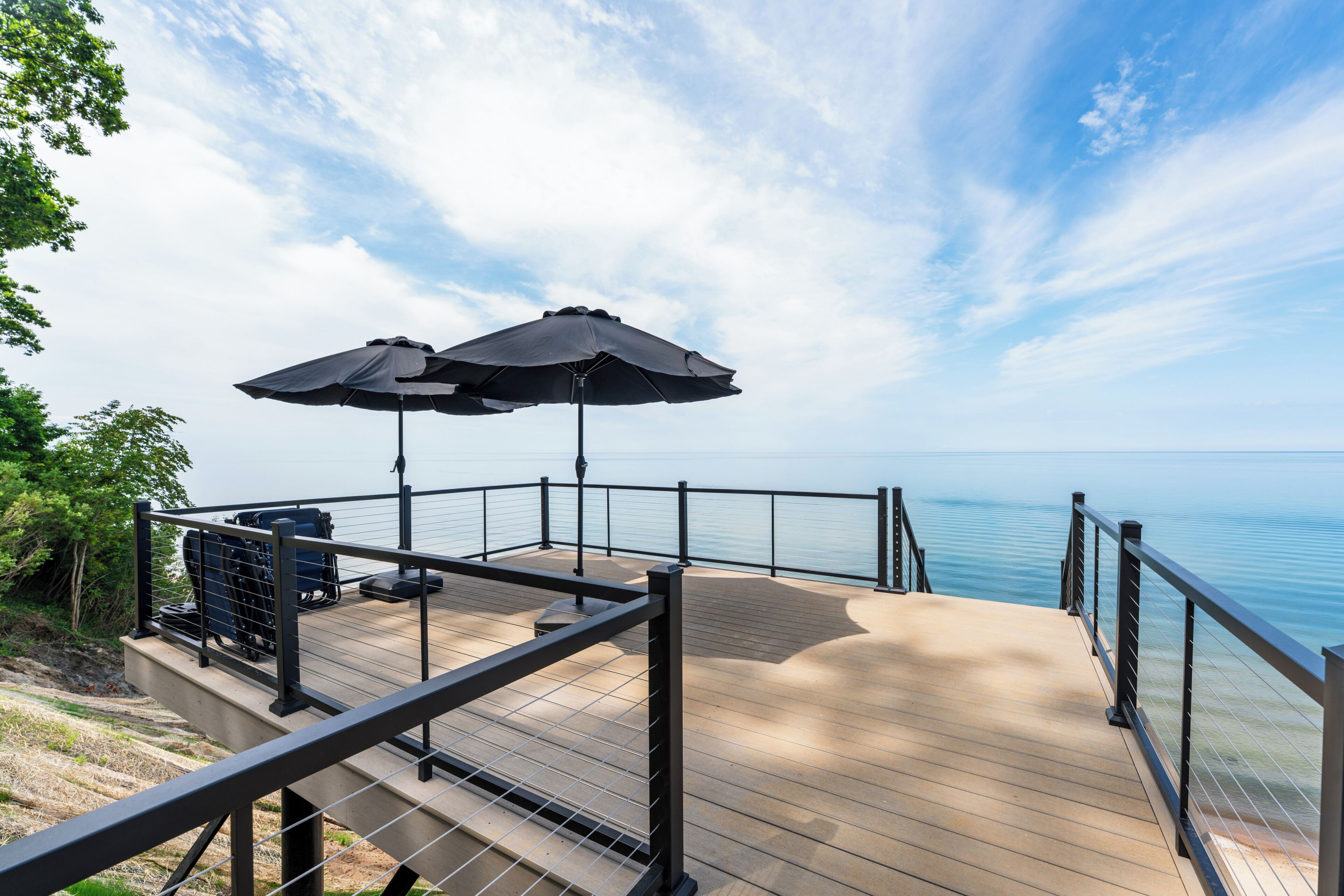 A deck with a railing overlooking a body of water, two umbrellas, and outdoor seating.