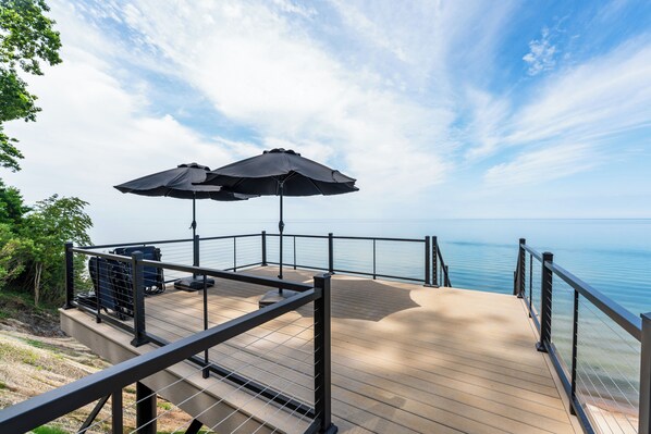 Eine Terrasse mit Geländer und Blick auf ein Gewässer, zwei Sonnenschirme und Sitzgelegenheiten im Freien.