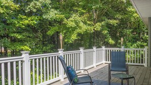 A covered outdoor deck with white railings, two wicker chairs, and a blue mat. - Bed & Birdie Near Golf Course & Downtown Saugatuck (Saugatuck)
