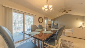 A dining area with a wooden table, chairs, and a chandelier. There is a ceiling fan and a fireplace in the background. - Bed & Birdie Near Golf Course & Downtown Saugatuck (Saugatuck)