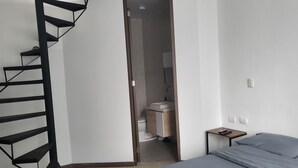 Un dormitorio moderno con una escalera espiral, una cama, una mesita de noche y un baño visible a través de una puerta abierta.