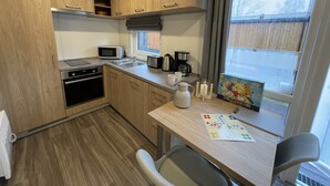 A compact kitchen with wooden cabinets, a microwave, a toaster, and a coffee maker. There is a window with a view of a fence outside. - Tiny Haus Sonnenschein by Interhome (Wemding)