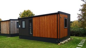 Un bâtiment moderne à deux étages, avec une combinaison de panneaux en bois foncé et clair, une porte en verre et une petite fenêtre.