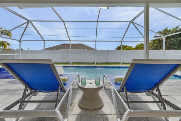 Un espace aménagé au bord de la piscine, avec deux chaises longues bleues et une table sur laquelle sont posés deux verres.