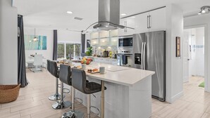 Een moderne keuken met een centraal eiland, roestvrijstalen apparatuur en een eethoek met barstoelen.