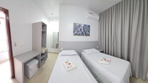Habitación de hotel con dos camas individuales, un escritorio, un armario y un cuadro en la pared.