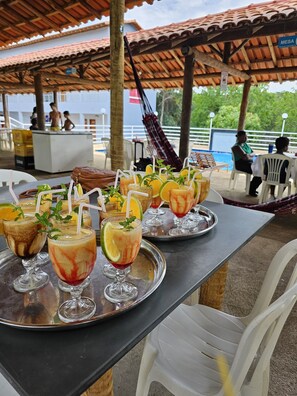 A covered outdoor dining area with tables set with drinks and a pool in the background. - Paraíso Pousada e Restaurante  (Minas Novas)