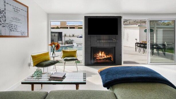 Una sala de estar moderna con chimenea, piscina y un comedor visible a través de puertas de vidrio.