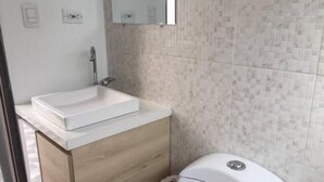 Un baño con un lavamanos blanco, tocador de madera y un inodoro.