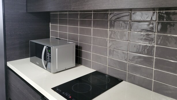 Una cocina moderna con microondas integrado, placa de inducción negra y salpicadero de azulejos gris oscuro.