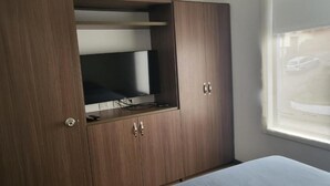 Un dormitorio con cama, armario con televisor incorporado y ventana con vista a un coche.
