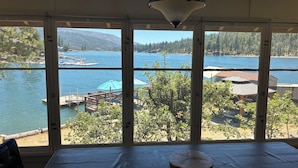 Quarto com uma grande janela com vista para um lago, uma mesa de madeira e um candeeiro pendente.