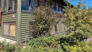 Uma cabana de toras moderna com janelas grandes, varanda coberta e um jardim bem cuidado.