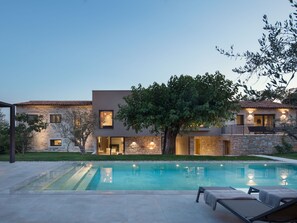 Une maison moderne à deux étages, dotée d’une piscine, de murs en pierre et d’un arbre dans le jardin.