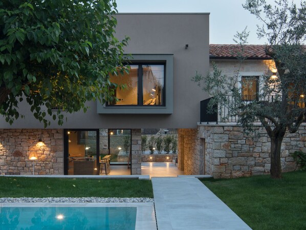 Une maison moderne à deux étages, dotée d’une façade en pierre, d’une piscine et d’un espace de détente extérieur.