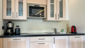A compact kitchen with light wood cabinets, a built-in oven, a coffee maker, and a kettle. - Appartement Disüdlöner (Sylt)