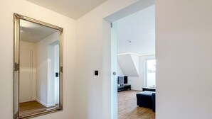 A hallway with a large mirror, a door leading to a living area with a TV, and a wooden floor. - Appartement Disüdlöner (Sylt)