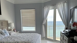 A bedroom with a bed, a ceiling fan, a large window with blinds, a view of the ocean, and a dresser with drawers. - Beautiful ocean view and beach front close to shopping downtown  (Panama City Beach)