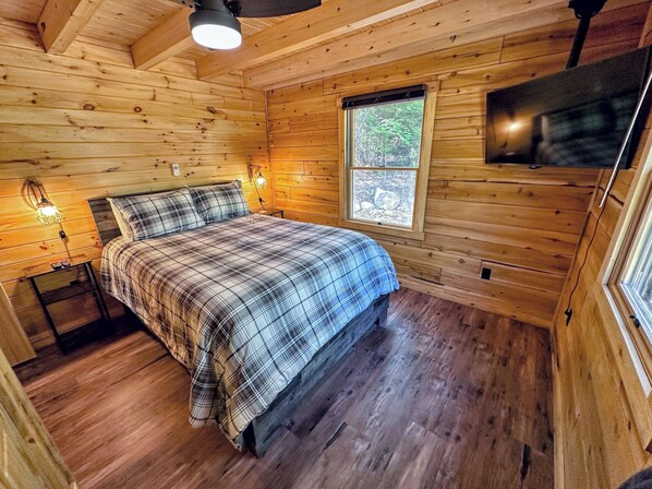 A wooden cabin bedroom with a bed, a window, and a wall-mounted TV.