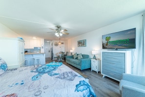 Un dormitorio con cama, ventilador de techo, kitchenette, comedor y sala de estar con televisor.