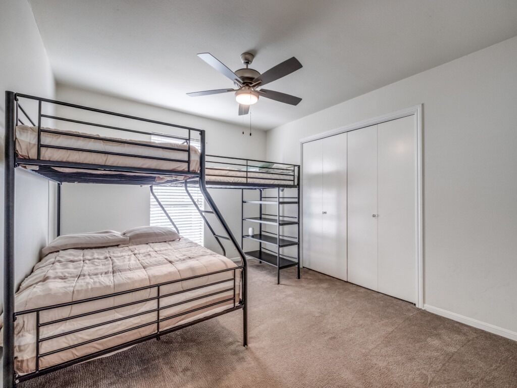 Une chambre avec un lit superposé, un ventilateur de plafond, une armoire et un sol recouvert de moquette.