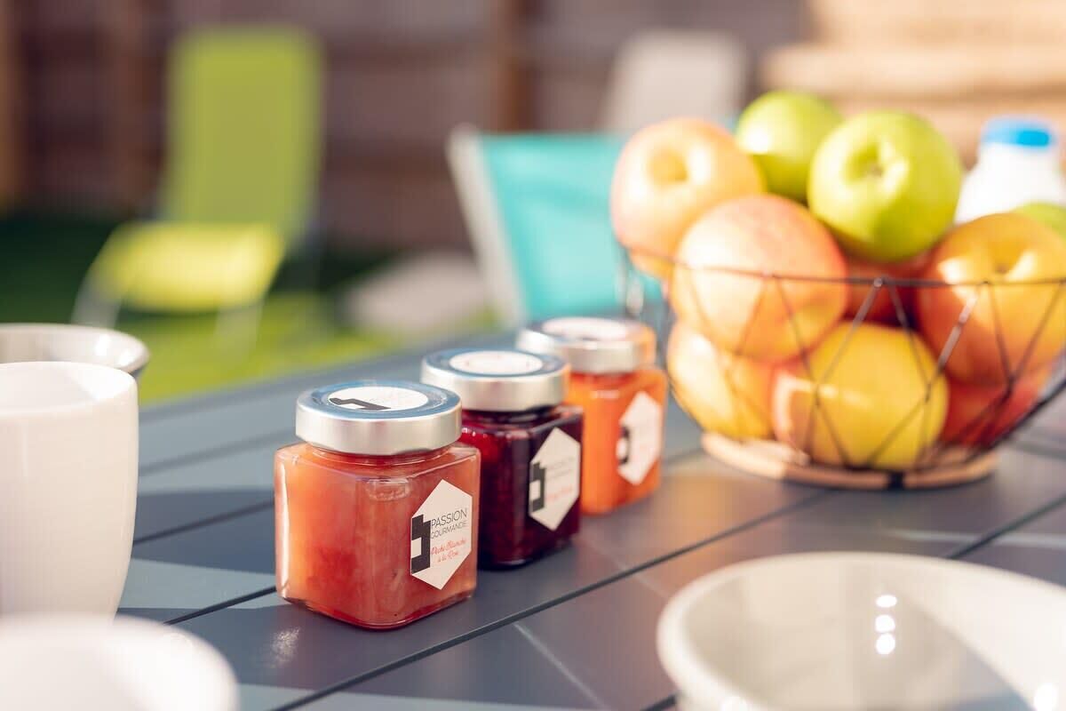 A table with jars of jam and a bowl of apples.