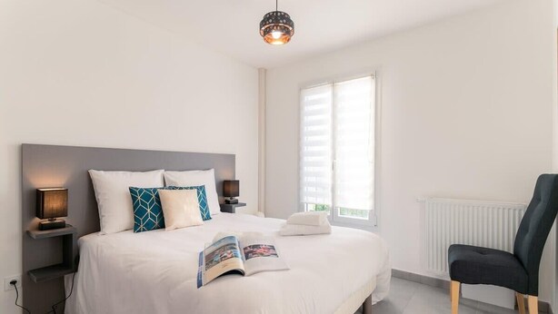 Ein modernes Schlafzimmer mit einem großen Bett, Nachttischlampen, einer Leselampe, einem Fenster mit Jalousien und einem Sessel.