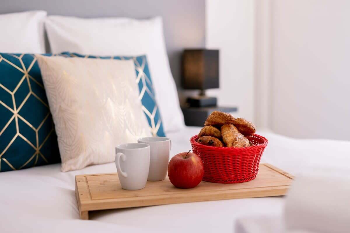 A neatly arranged breakfast tray on a bed with pillows, a lamp, and a nightstand.