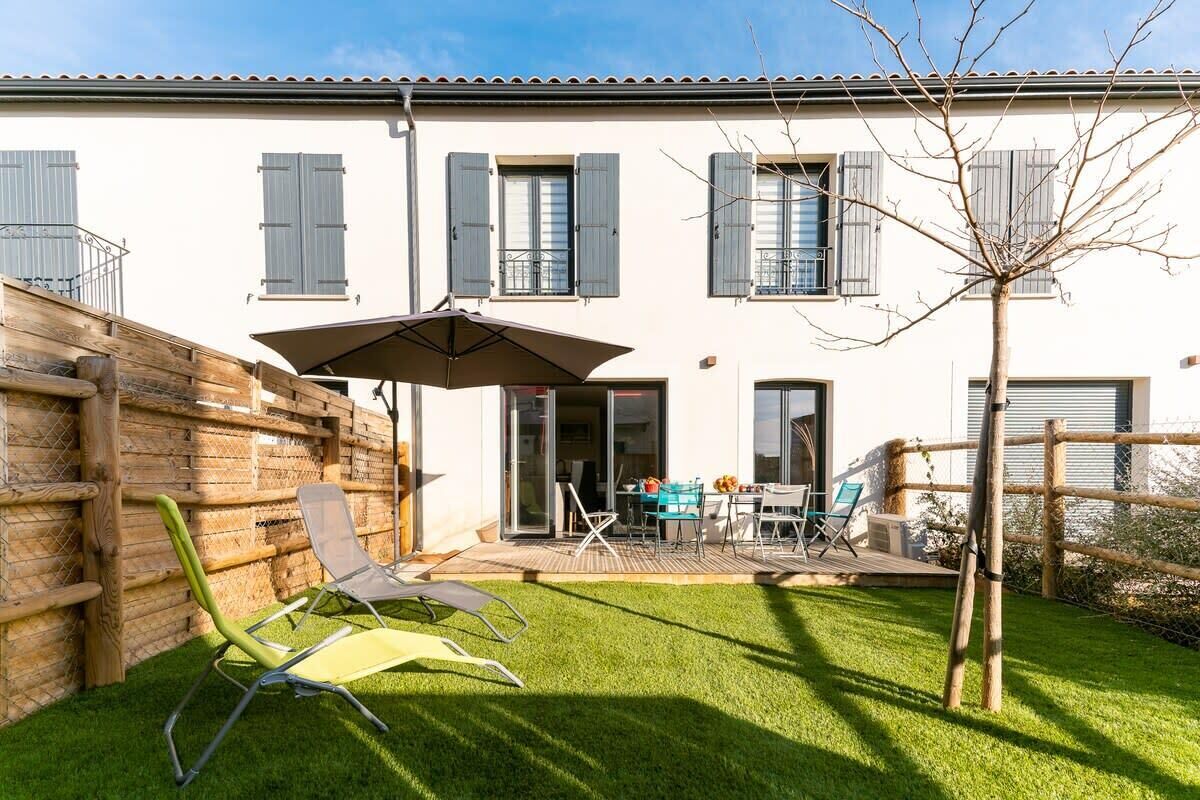 Une maison à deux étages dotée d’un patio aménagé avec des meubles d’extérieur et un arbre.