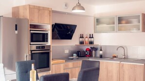 Eine moderne Küche mit Holzausstattung, einer eingebauten Mikrowelle, einem Backofen und einer Kaffeemaschine. Ein Essbereich mit Tisch und Stühlen ist ebenfalls vorhanden.
