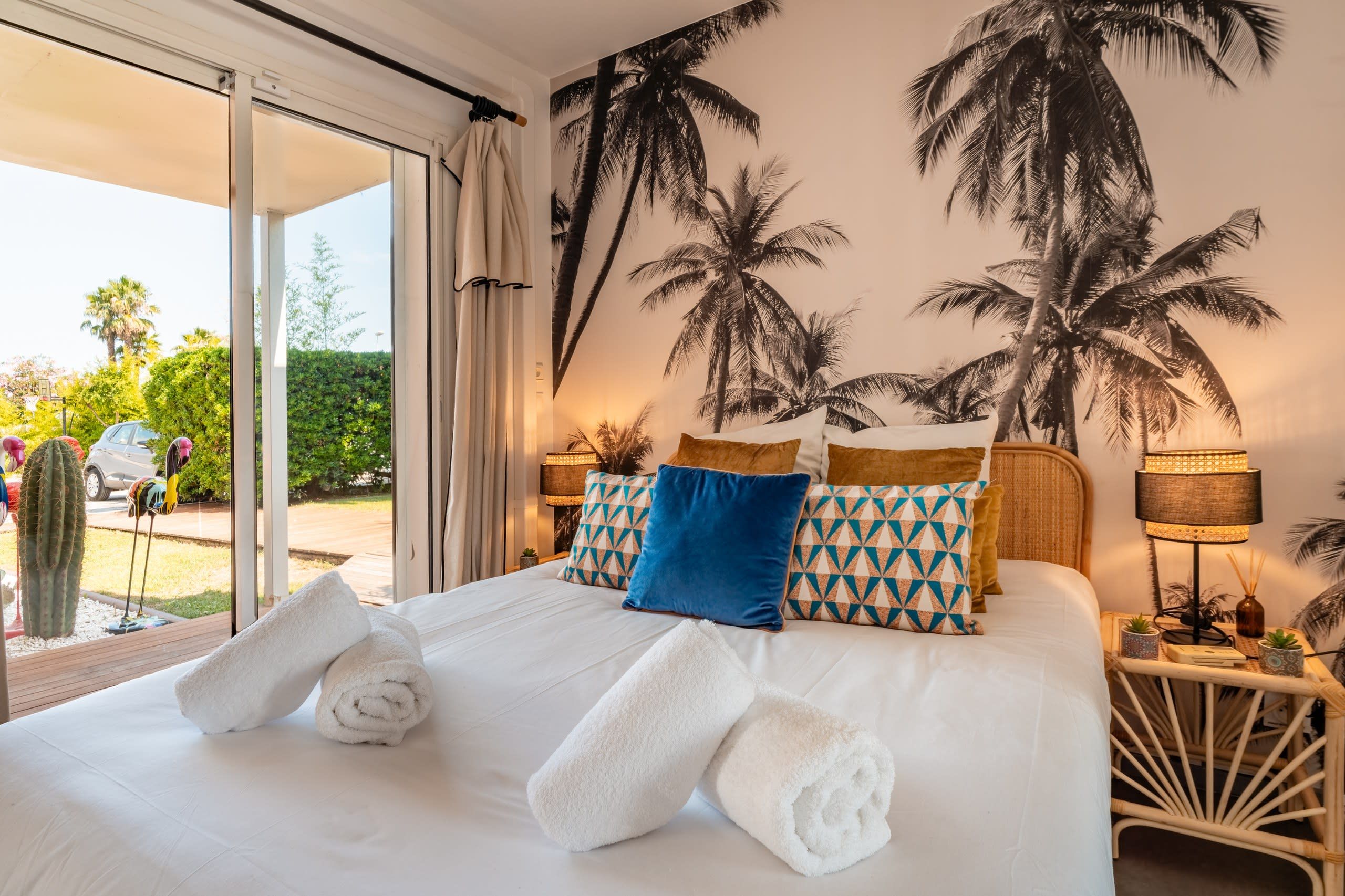 Een hotelkamer met een bed, kussens, een nachtkastje, een lamp en uitzicht op het landschap.