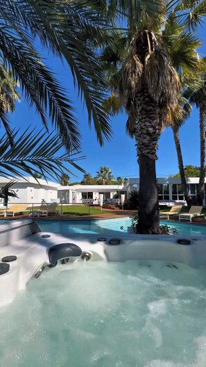 A pool area with a hot tub, lounge chairs, and palm trees.