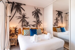 Une chambre avec un grand lit, un miroir et une fresque murale représentant des palmiers.