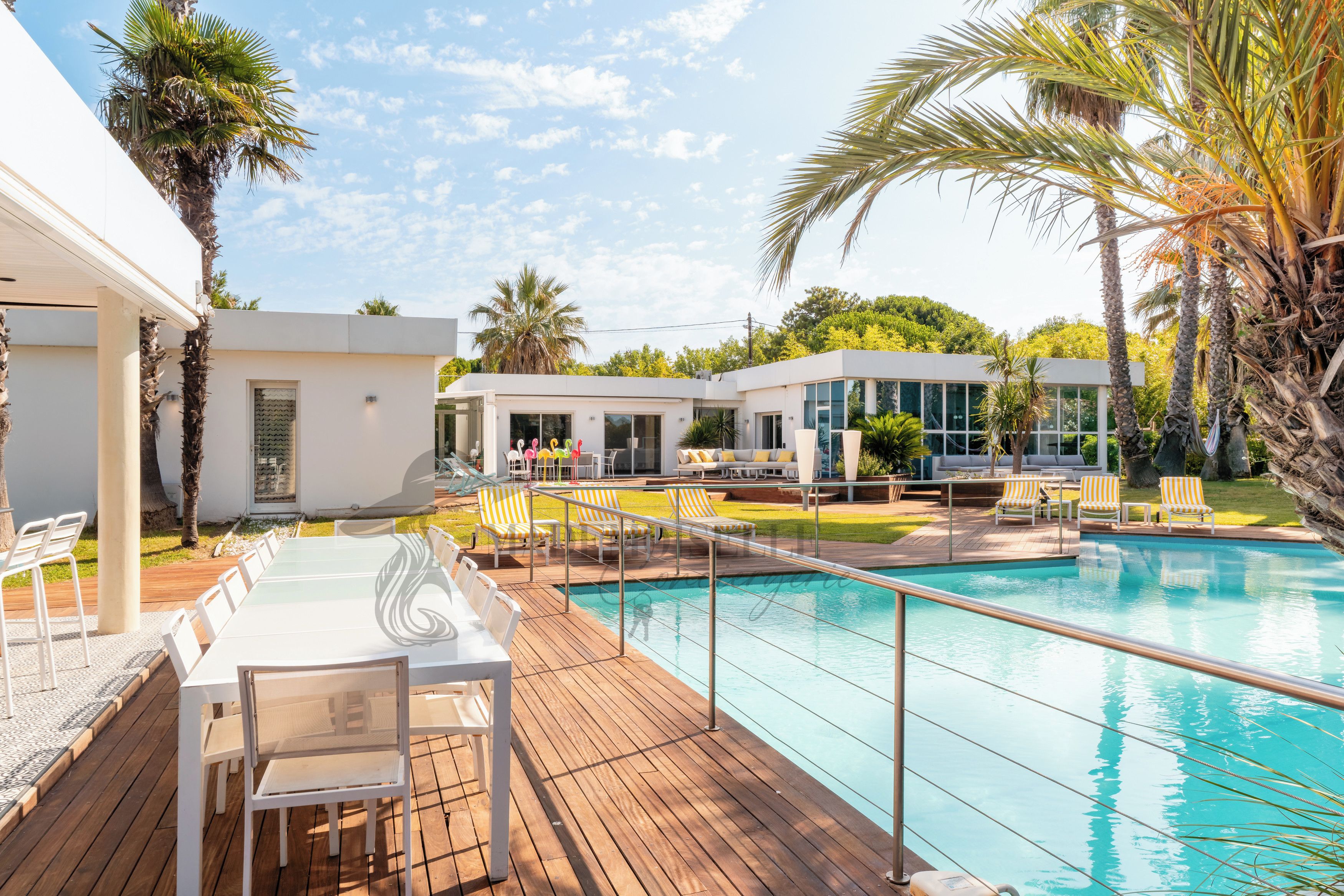 A pool area with a wooden deck, lounge chairs, and a modern building with large windows.