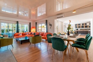 Een ruime woonkamer met een grote bank, een eettafel voor zes personen en een keuken op de achtergrond.