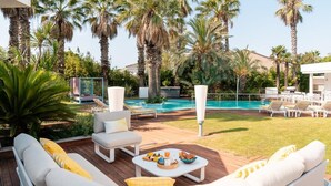 A poolside area with lounge chairs, a dining table with food, and a pool surrounded by palm trees. - Villa Summer Wind - Palm Beach Agathois (Agde)