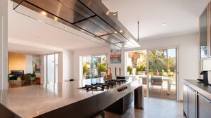 A modern kitchen with a central island, stainless steel appliances, and a view to an outdoor patio. - Villa Summer Wind - Palm Beach Agathois (Agde)