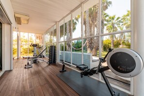 A gym with exercise equipment, large windows, and a view of palm trees.