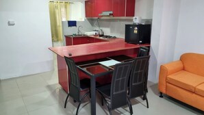 Cocina compacta con armarios rojos, estufa a gas, pileta y refrigerador negro. En la zona de estar, hay una mesa de comedor con sillas y un sofá naranja.